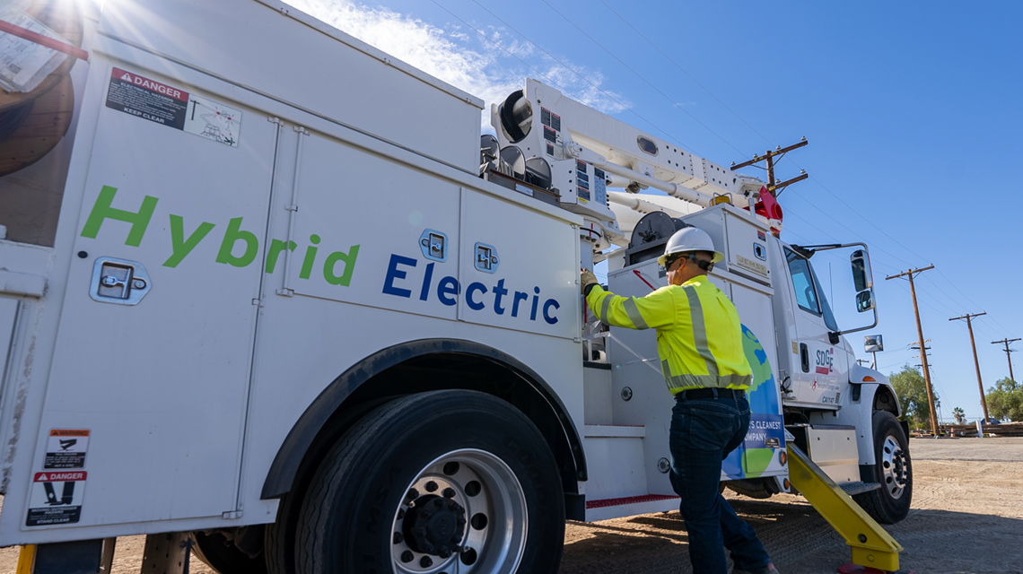 A team member stands next to one of SDG&E's hybrid electric fleet trucks