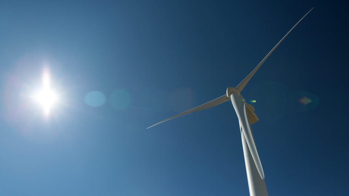 A single white wind turbine against bright blue sky