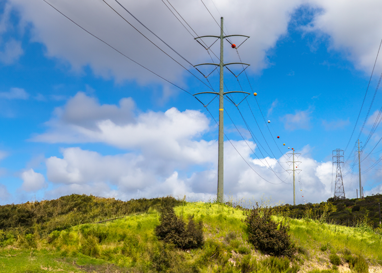 Power lines in California atop a grassy hill against a blue sky with some clouds